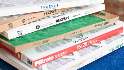 A stack of various 16x25x1 inch furnace filters in different brands and packaging, placed on a blue surface—perfect for routine furnace maintenance.