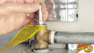 %Imagetitle% | Any Hour Services A hand lifts the lever on a brass valve connected to a water heater pipe, with a yellow warning tag attached—a crucial step in water heater safety to help prevent water heater explosion.