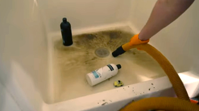 %Imagetitle% | Any Hour Services A person uses a hose to clean a dirty bathtub filled with dark residue and scattered bottles, possibly addressing common plumbing problems or recent plumbing repair.