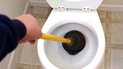 %Imagetitle% | Any Hour Services A person uses a plunger to unclog a white toilet, tackling one of the most common plumbing problems.