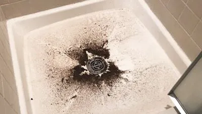 %Title% | Any Hour Services A white shower floor with dirty black sludge splattered around and inside the drain, suggesting a drainage or plumbing issue that may require professional plumbers or essential plumbing tips to resolve.