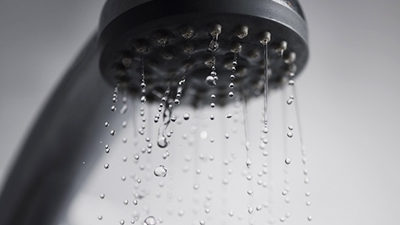 %Imagetitle% | Any Hour Services Close-up of a showerhead with water droplets flowing out of the nozzles against a blurred background, highlighting potential common plumbing problems that may require plumbing repair.