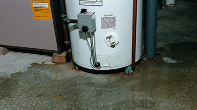 %Imagetitle% | Any Hour Services A water heater with visible rust and water stains on the basement floor, highlighting common plumbing problems that may require immediate plumbing repair.