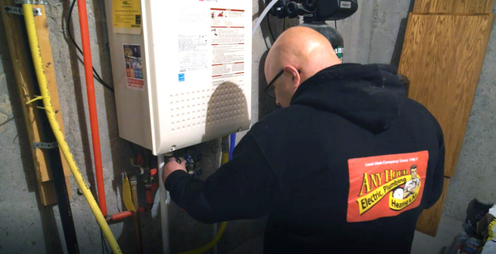 A technician in a branded hoodie works on a wall-mounted tankless water heater in a utility room, carefully weighing the pros and cons of upgrading to this efficient system.