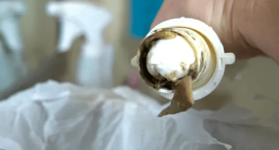 %Imagetitle% | Any Hour Services A close-up of a dirty washing machine filter being held over a trash bag, with visible lint and debris stuck to it—similar to kitchen sink drain cleaning needed to remove odor from sink.