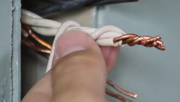 %Focuskw% | Any Hour Services A close-up of a hand twisting together exposed copper electrical wires inside a metal junction box, showcasing a basic electrical DIY electrical project.