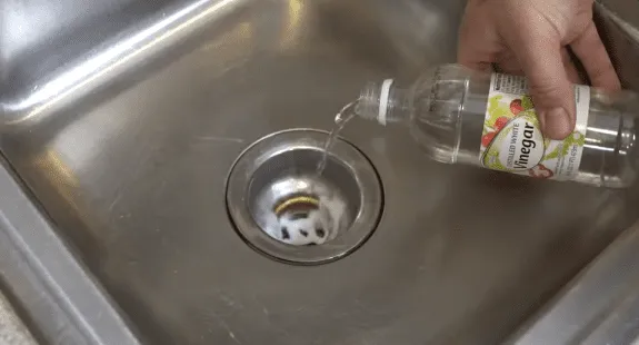 %Imagetitle% | Any Hour Services A hand pours vinegar from a bottle into a kitchen sink drain, demonstrating how to clean sink drain and freshen up a smelly kitchen sink.