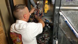 %Title% | Any Hour Services A technician in a white shirt repairs or inspects electrical components inside an HVAC unit, using tools and testing equipment as part of thorough furnace maintenance.