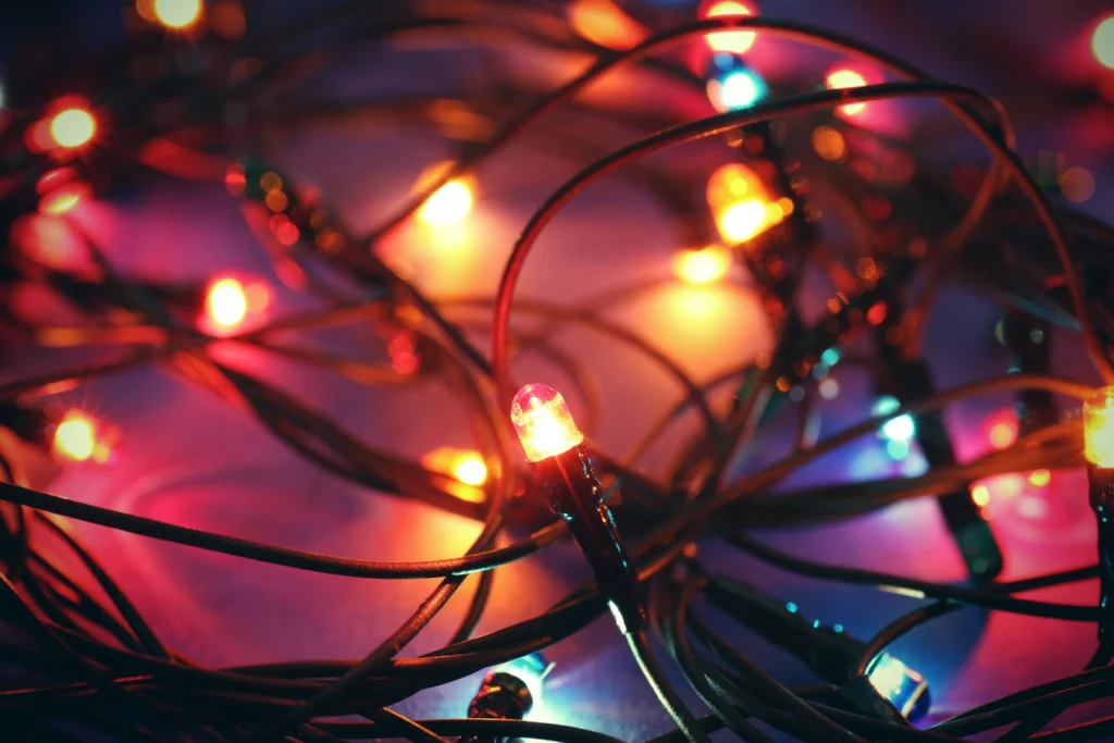 A close-up of tangled Christmas lights with glowing bulbs in red, orange, blue, and yellow adds festive sparkle against a blurred background.