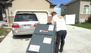 %Title% | Any Hour Services A person in uniform moves a large metal appliance on a dolly up the driveway toward a house with a parked minivan.