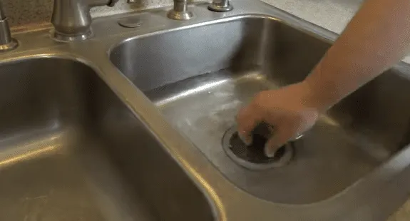 %Imagetitle% | Any Hour Services A person places a rubber drain stopper into the drain hole of a stainless steel kitchen sink as part of their kitchen sink cleaning routine.