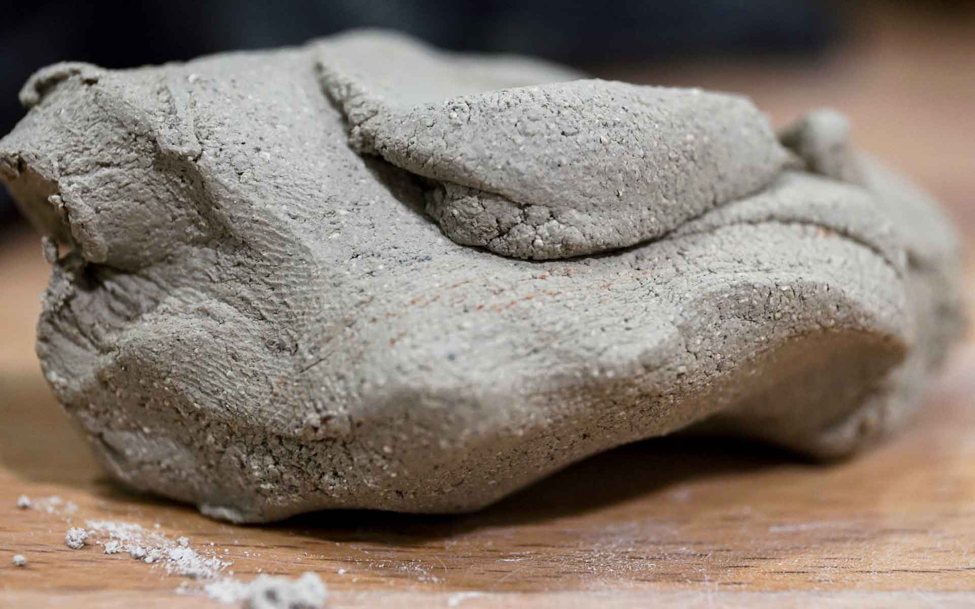 A close-up view of a lump of gray modeling clay resting on a wooden surface, resembling the texture and appearance of common sewer materials used in various sewer pipe types.
