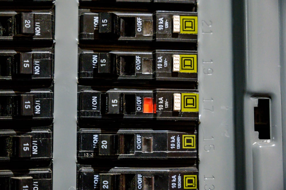 Close-up view of a circuit breaker panel with one breaker switch showing a red indicator, an electrical sign of a possible home electrical problem, while others remain in the "on" position.