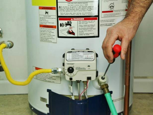 A person performs maintenance on a water heater, using a screwdriver to adjust or repair the control panel with warning labels visible, helping to extend its lifespan.