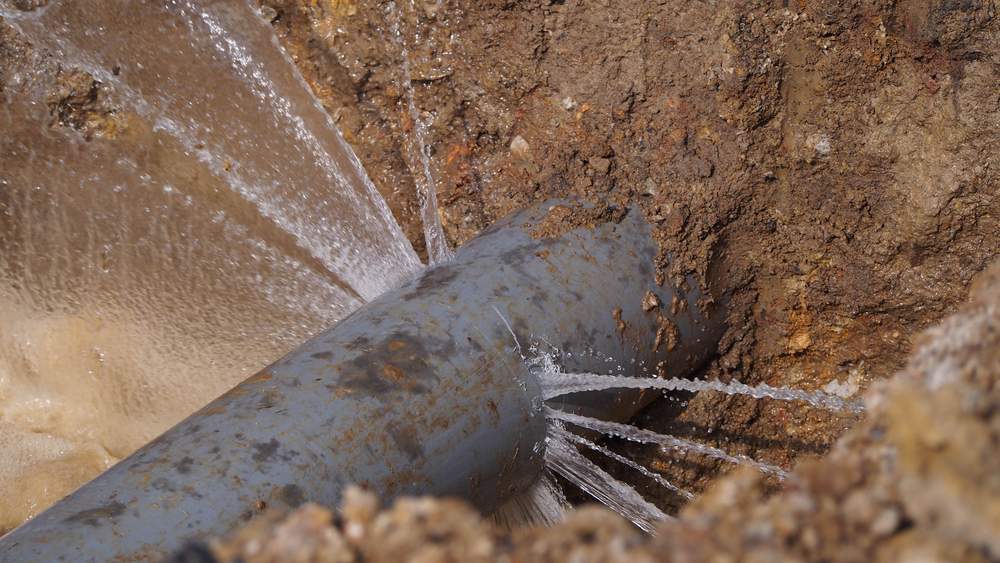 %Title% | Any Hour Services A close-up view of a damaged sewer pipe failure, with several streams of water spraying out through multiple cracks and holes.