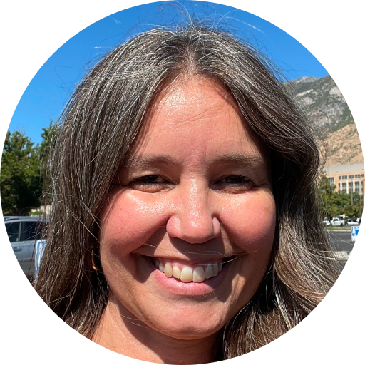 A woman with long brown and gray hair smiles outdoors during a Summer Sweepstakes, with trees, cars, and mountains in the background under a blue sky.