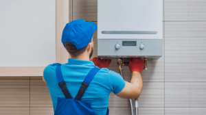 A technician in blue uniform and red gloves works on a wall-mounted gas boiler in a tiled room, adjusting the controls after a water heater failure leaves an Arizona home with no hot water.